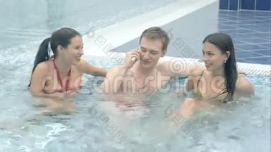 两个漂亮的<strong>女人</strong>嘲笑那个在游泳池里放松的年轻人<strong>接电话</strong>